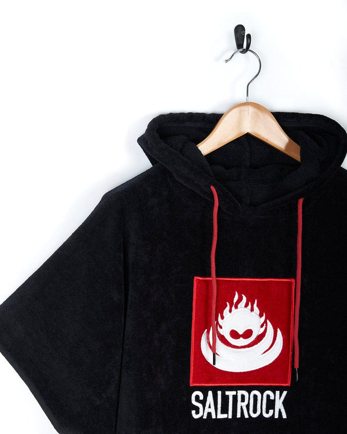 Black Corp Changing Towel with red and white Saltrock logo, made from absorbent cotton towelling material, hanging on a hook against a white background.