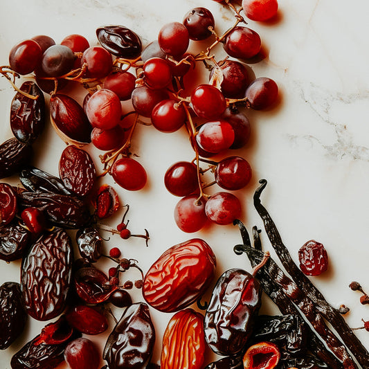 An assortment of dried fruits and fresh grapes, along with vanilla beans, arranged on a marble surface.