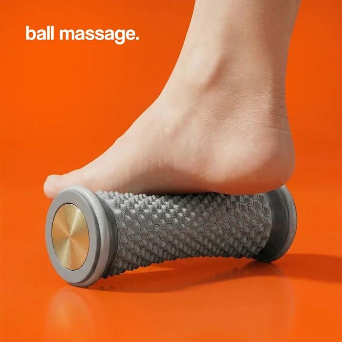 Gray massage roller with textured surface and gold accents, positioned under a foot on an orange background.