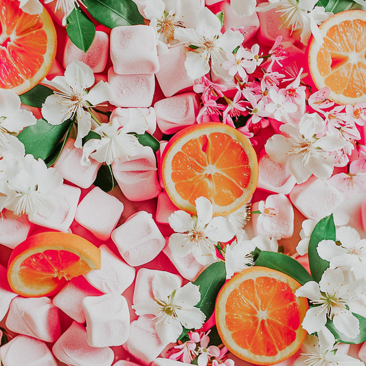 A colorful fragrance oil product image featuring slices of orange and marshmallows with white flowers on a pink background.