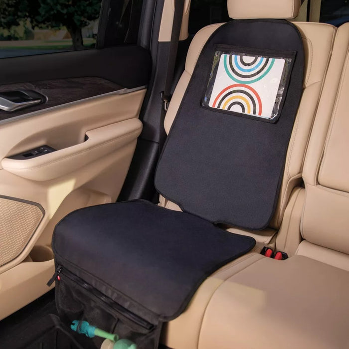 The Nuby Safe in the Seat Car Seat Protector fits rear and forward-facing seats, with a clear pocket displaying a colorful tablet cover and a storage pouch at the bottom holding a green bottle, shown on a beige back seat.