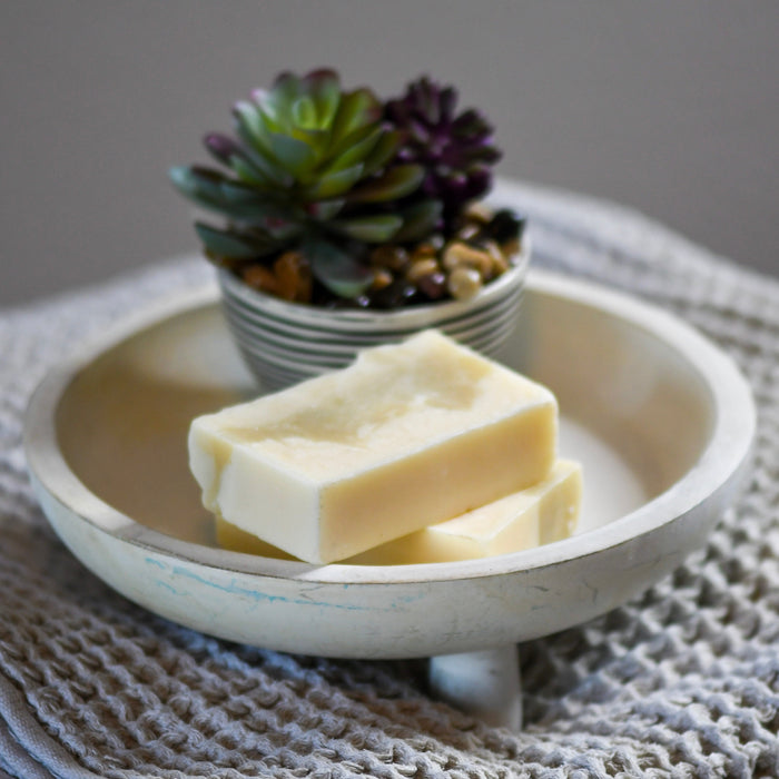 A raw bar of Simply Hypnotic Organic Soap with Geranium, Cedarwood & Patchouli Essential Oils, displayed in a white bowl with a knitted texture in the background.