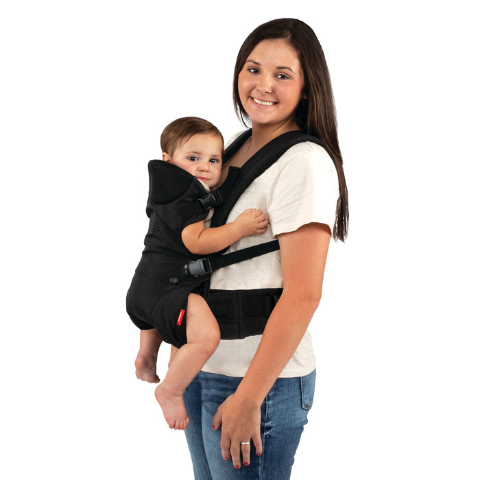 A woman in a white shirt and jeans smiles while carrying her baby in the Nuby SureFit Baby Carrier, which adjusts easily to keep the baby secure and comfortable as they rest contentedly against her chest against a white background.